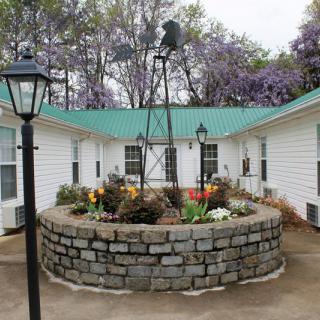 A quaint courtyard with a central garden surrounded by a stone brick wall, featuring colorful flowers and a decorative windmill.