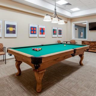 A well-appointed billiards room featuring a pool table, chairs, and framed artwork on the walls.