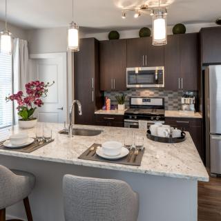 A modern kitchen featuring dark cabinets, stainless steel appliances, and a marble countertop with bar seating.