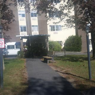 A view of a residential building with a pathway surrounded by grass and trees.