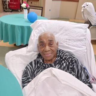 An elderly person smiling from their bed in a care facility.