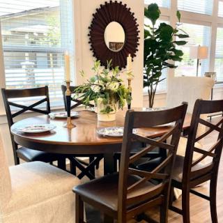 A stylish dining area featuring a round wooden table, elegant chairs, a decorative mirror, and greenery.