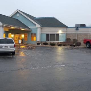 A view of a hotel entrance in the evening, featuring parked cars and a cloudy sky.