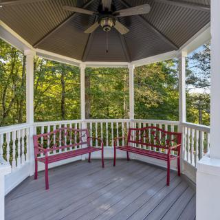 A peaceful gazebo with red benches and a ceiling fan, surrounded by trees.