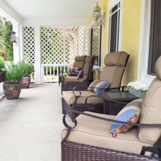 A cozy porch with wicker chairs and cushions, decorated with plants for a relaxing outdoor retreat.