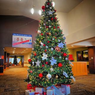 A beautifully decorated Christmas tree adorned with ornaments and surrounded by presents, set in a festive indoor space.