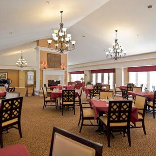 A spacious and well-lit dining area with elegantly arranged tables and chairs, featuring chandeliers and warm decor.