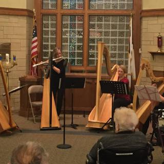 A group of musicians performs on harps in a cozy indoor setting, engaging an attentive audience.