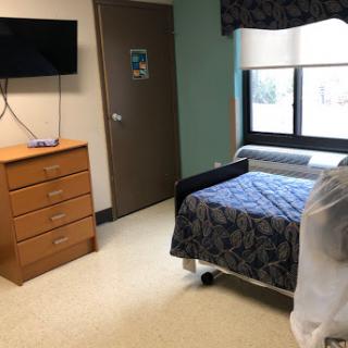 A hospital room featuring a patient bed, dresser, and television, with natural light coming through the window.