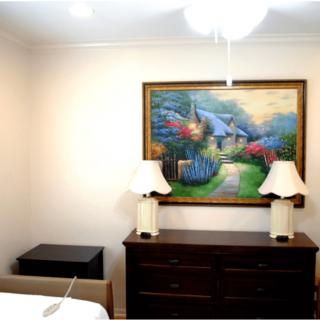 A bedroom with a dresser, two lamps, and a colorful landscape painting on the wall.