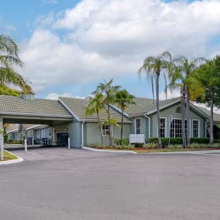 A suburban residential building with palm trees and a driveway under a cloudy sky.