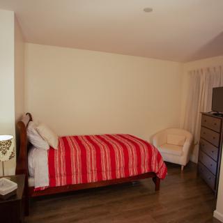 A cozy bedroom with a single bed covered in a red-striped blanket, wooden flooring, and simple furnishings.