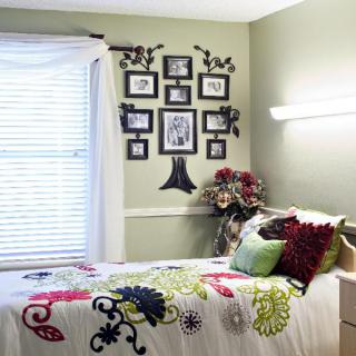 A cozy bedroom with floral patterned bedding and a wall decorated with framed photos and art.