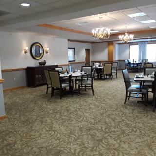 An elegantly decorated dining room with multiple tables and chairs, featuring chandeliers and carpeted floors.