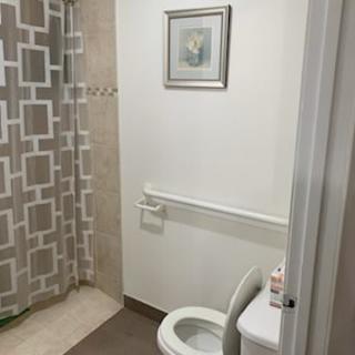 A clean, minimalistic bathroom featuring a toilet, shower with a patterned curtain, and wall art.