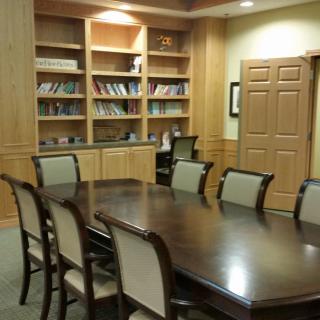 A conference room with a large table, surrounded by chairs and bookshelves.