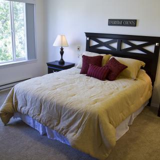 A cozy bedroom with a neatly made bed, decorative pillows, and a bedside lamp.
