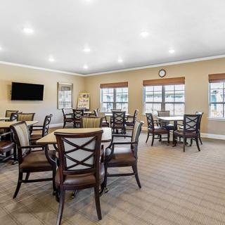 A spacious dining area with multiple tables and chairs, featuring large windows and a wall-mounted television.