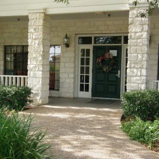 A welcoming front porch with stone columns and a green door, surrounded by lush landscaping.