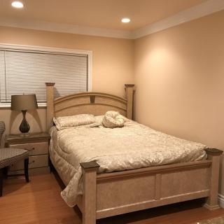 A cozy bedroom with beige walls, featuring a bed, nightstand, and lamp.