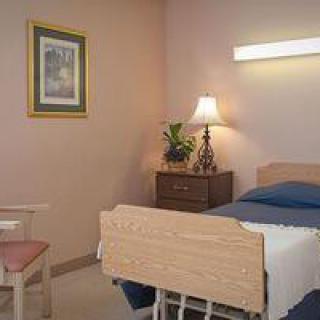 A hospital room with a bed, nightstand, and lamp by the side.