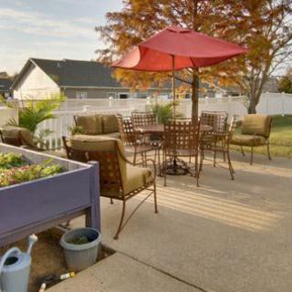 A cozy backyard patio with furniture and a red umbrella, set against an autumn backdrop.