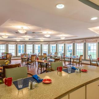 A cozy dining room with multiple tables and large windows letting in natural light.
