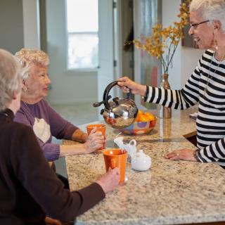 Three seniors enjoying tea and conversation in the kitchen.