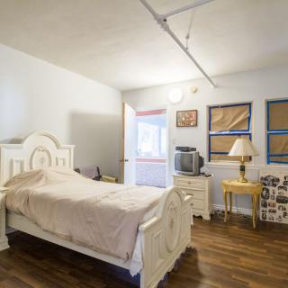 A neatly organized bedroom with a bed, nightstand, lamp, and television.