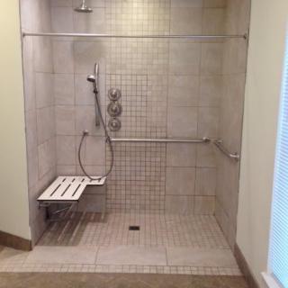 An accessible walk-in shower with tiled walls, a handheld shower head, foldable seat, and grab bars.