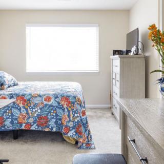 A cozy bedroom featuring a bed with floral bedding, a dresser, and a bright window.