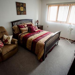 A cozy bedroom with a neatly made bed, armchair, and window allowing natural light.
