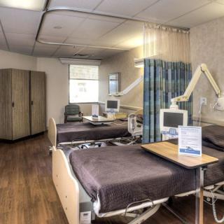 A hospital room with two beds and medical equipment, separated by privacy curtains.
