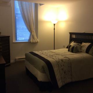 A cozy bedroom with a neatly made bed, a floor lamp, and a window with curtains.