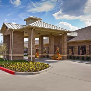 A welcoming entrance to a modern commercial building, surrounded by colorful landscaping and under a partly cloudy sky.