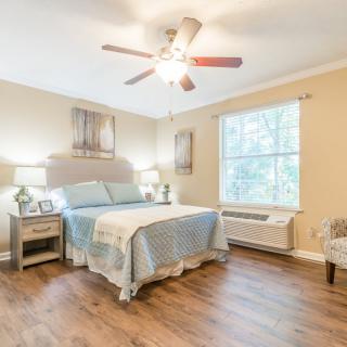 A cozy bedroom with hardwood flooring, featuring a bed with light blue bedding, two bedside tables with lamps, and a ceiling fan.
