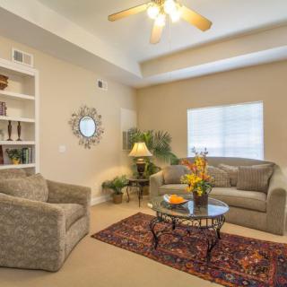A cozy living room with a comfortable sofa and armchair, a coffee table with flowers, and a bookshelf for decoration.