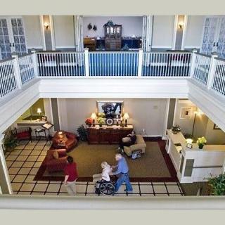 A spacious lobby in a nursing home with people, including one in a wheelchair, moving through the area.