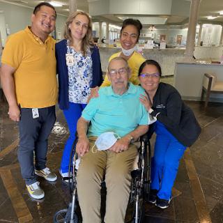 A cheerful group of caregivers posing with an elderly man in a wheelchair at a healthcare facility.
