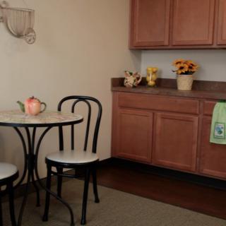 A cozy kitchen corner with a small table and chairs, adorned with a teapot and floral decorations.