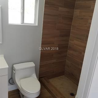 A modern minimalist bathroom featuring a toilet and a walk-in shower with wood-like tile.