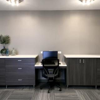 A minimalist office setup with a desk, chair, and computer between two cabinets.