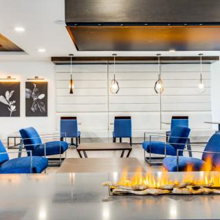 A modern lobby featuring blue chairs, a fireplace, and minimalist artwork.