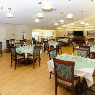 A well-lit dining room with multiple set tables and chairs on a wooden floor.