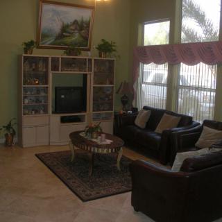 A cozy living room featuring a leather sofa, coffee table, entertainment center with a TV, and large windows allowing natural light to fill the space.