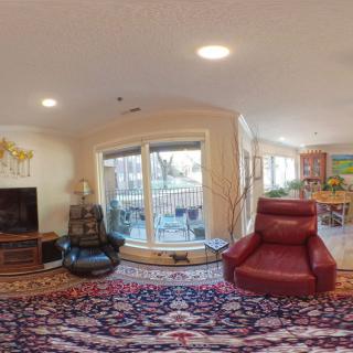 A comfortable living room with armchairs, a television, and large windows leading to a balcony.