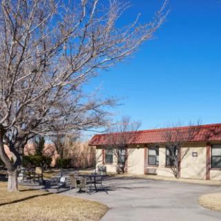 A park area featuring a building with a red roof, benches, and leafless trees under a clear blue sky.