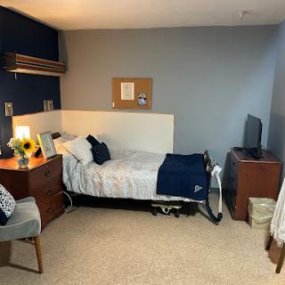A cozy and minimalist bedroom featuring a single bed, desk, and television.