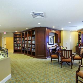 A cozy library with bookshelves, a reading area with chairs, and carpeted flooring.