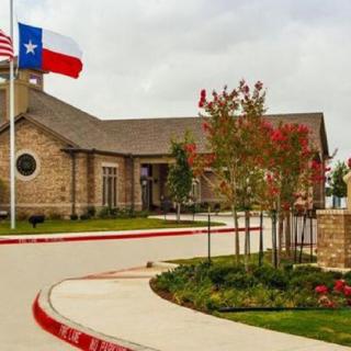 A building with a Texas flag in front, surrounded by landscaping and a cloudy sky.
